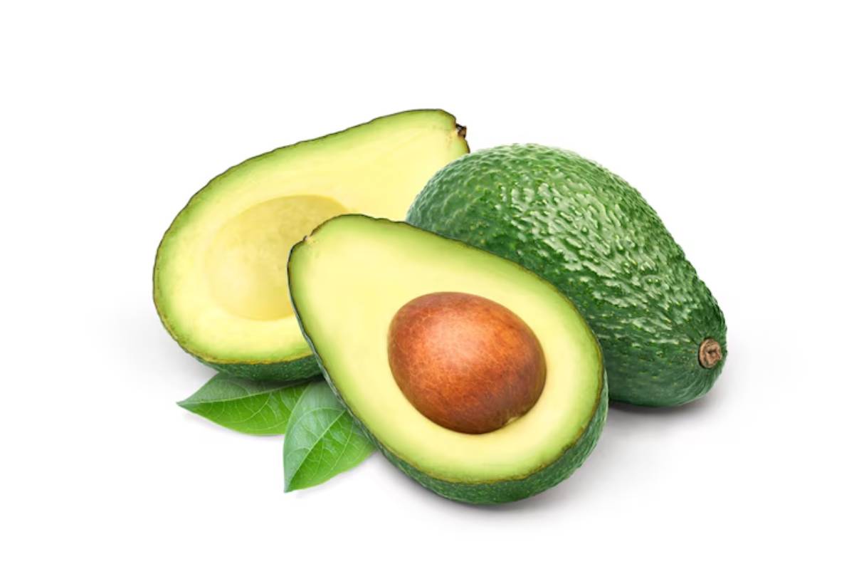 A halved avocado with a brown seed, alongside a whole avocado and green leaves on a white background.