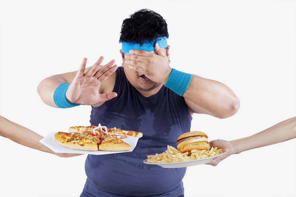 A person wearing exercise gear, sweating, is resisting two hands offering unhealthy food: pizza and a burger with fries.