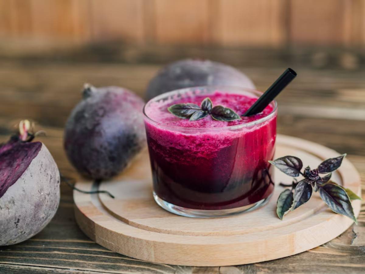 A vibrant beetroot smoothie garnished with fresh basil leaves, surrounded by whole beetroots on a wooden serving board.