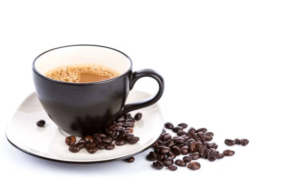 A black coffee cup filled with frothy beverage, resting on a white saucer, surrounded by scattered coffee beans.