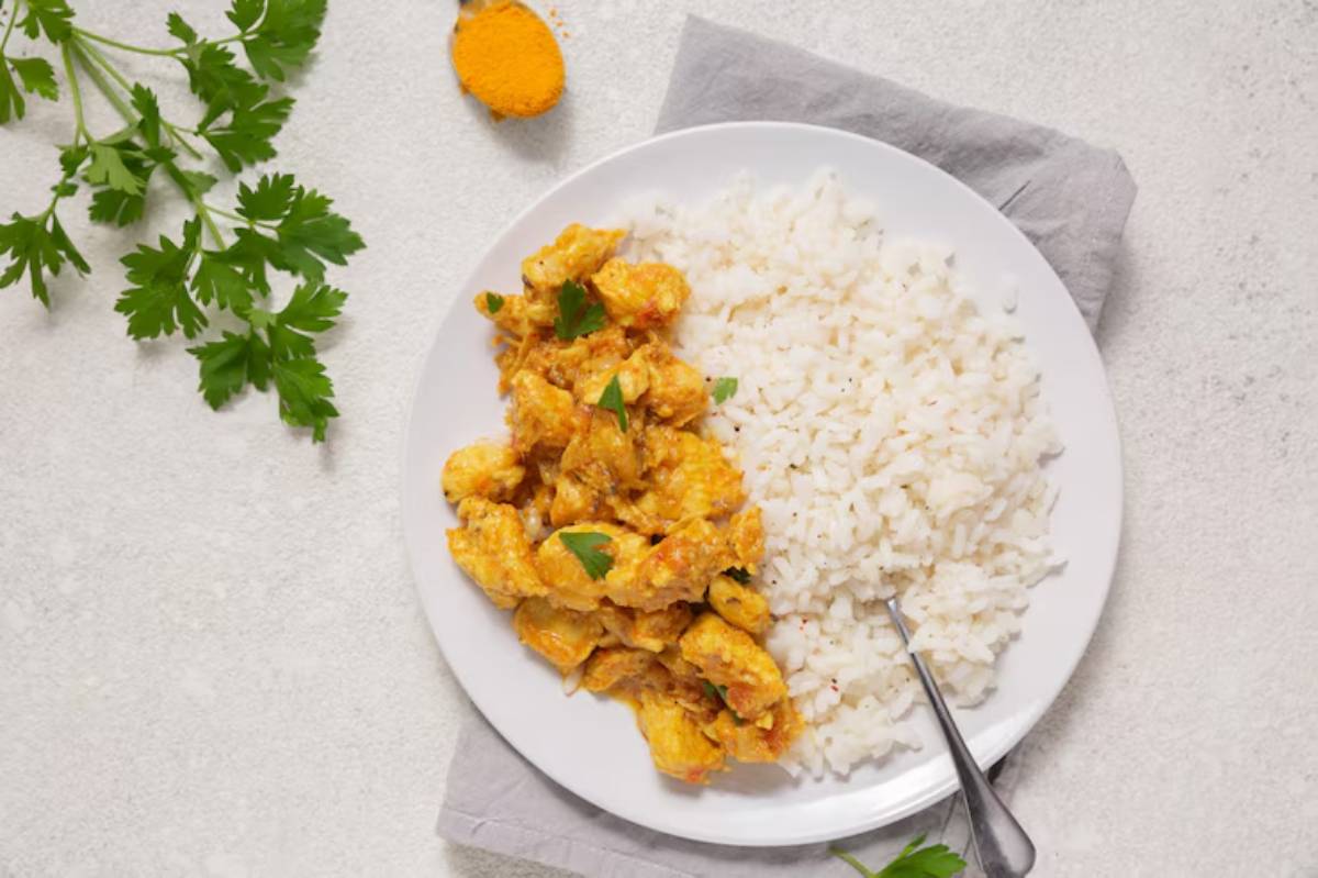 A plate of creamy chicken curry garnished with cilantro, served alongside fluffy white rice and a spoon, on a light background.