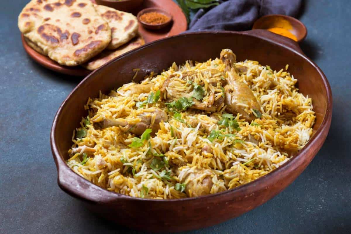 A clay pot filled with fragrant biryani, featuring tender chicken pieces garnished with coriander, alongside naan bread and spices.