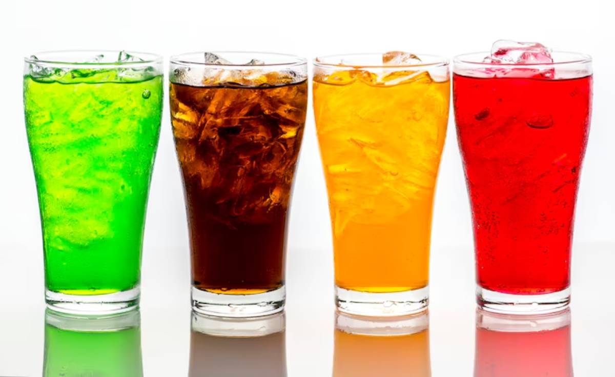 Four glasses of colorful beverages green, brown, yellow, and red, filled with ice cubes, arranged in a row against a white background.