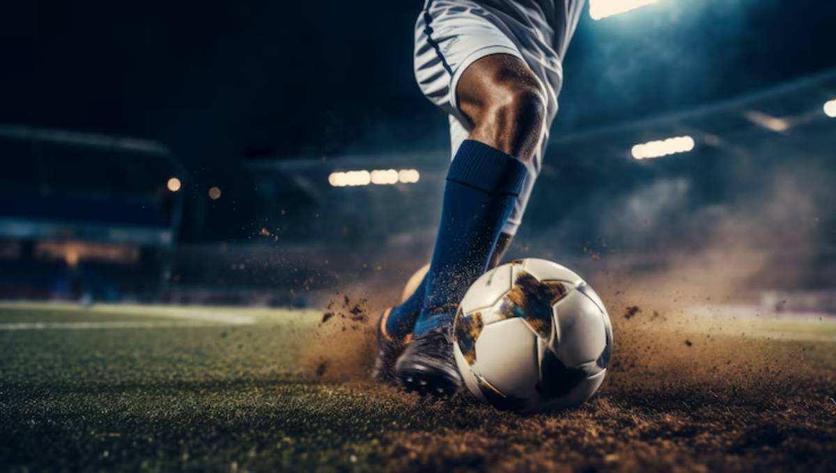 A soccer player's leg striking a ball on a field, kicking up dust under stadium lights during a game at night.