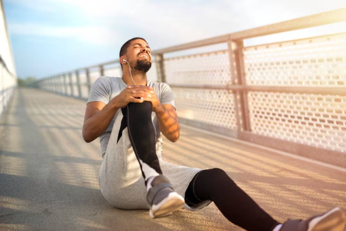 A man in athletic wear sits on a bridge, stretching his legs while listening to music, with sunlight illuminating the scene.