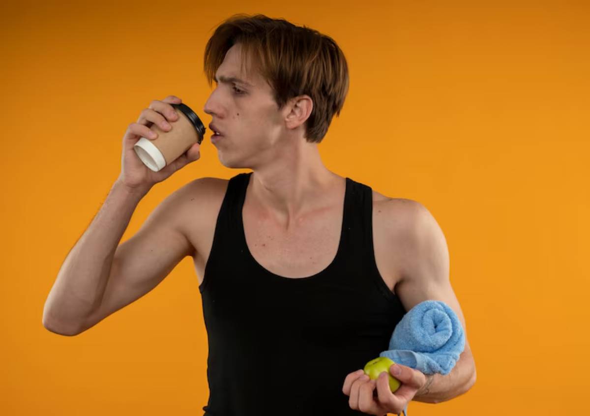 A person in a black tank top holds a coffee cup, a green apple, and a blue towel against a vibrant orange background.