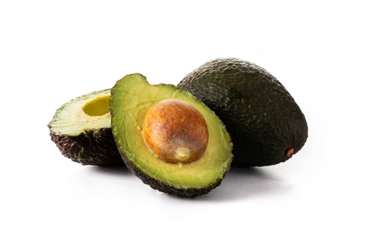 A halved avocado showcases its creamy green flesh and brown pit, accompanied by a whole avocado on a white background.