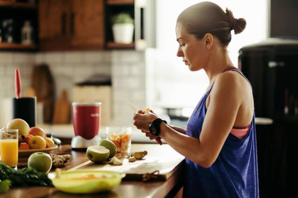 A person in a kitchen preparing fresh fruits and vegetables, with a blender and ingredients laid out on the counter.