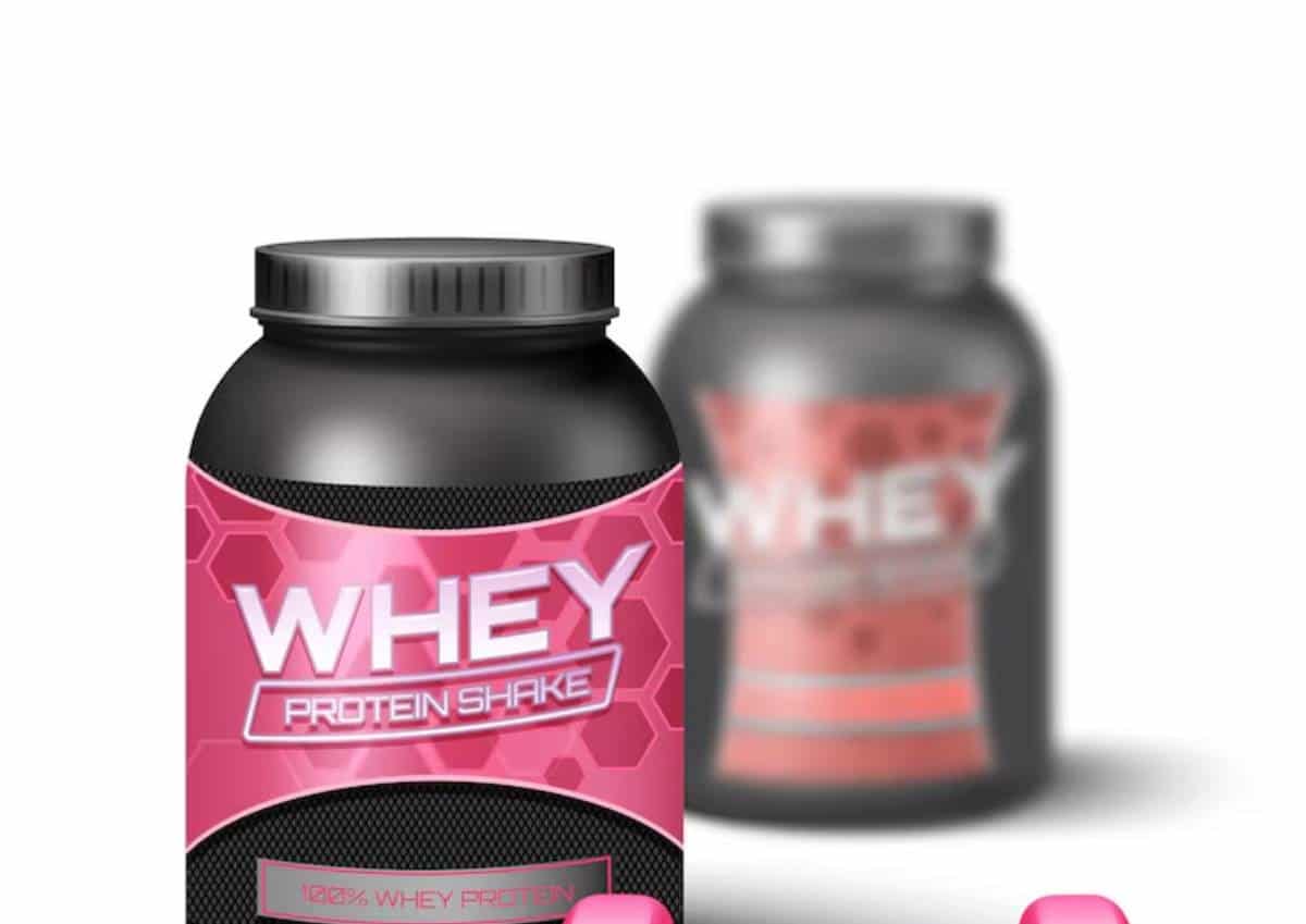 A pink and black protein shake container labeled WHEY PROTEIN SHAKE with a 100% whey protein badge, set against a blurred background.